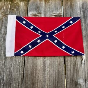 6x9 inch Confederate battle flag with a white sleeve, laid flat on a weathered wooden surface, showing the red background, navy blue St. Andrew’s cross, and thirteen white stars.