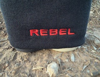 Back view of black beanie with bold red embroidered text reading "REBEL" stitched into the cuff.
