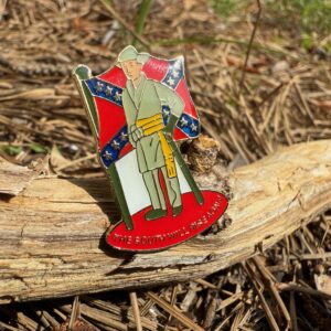 Confederate soldier enamel lapel pin with Rebel battle flag background and "The South Will Rise Again" slogan, displayed on natural wood outdoors.