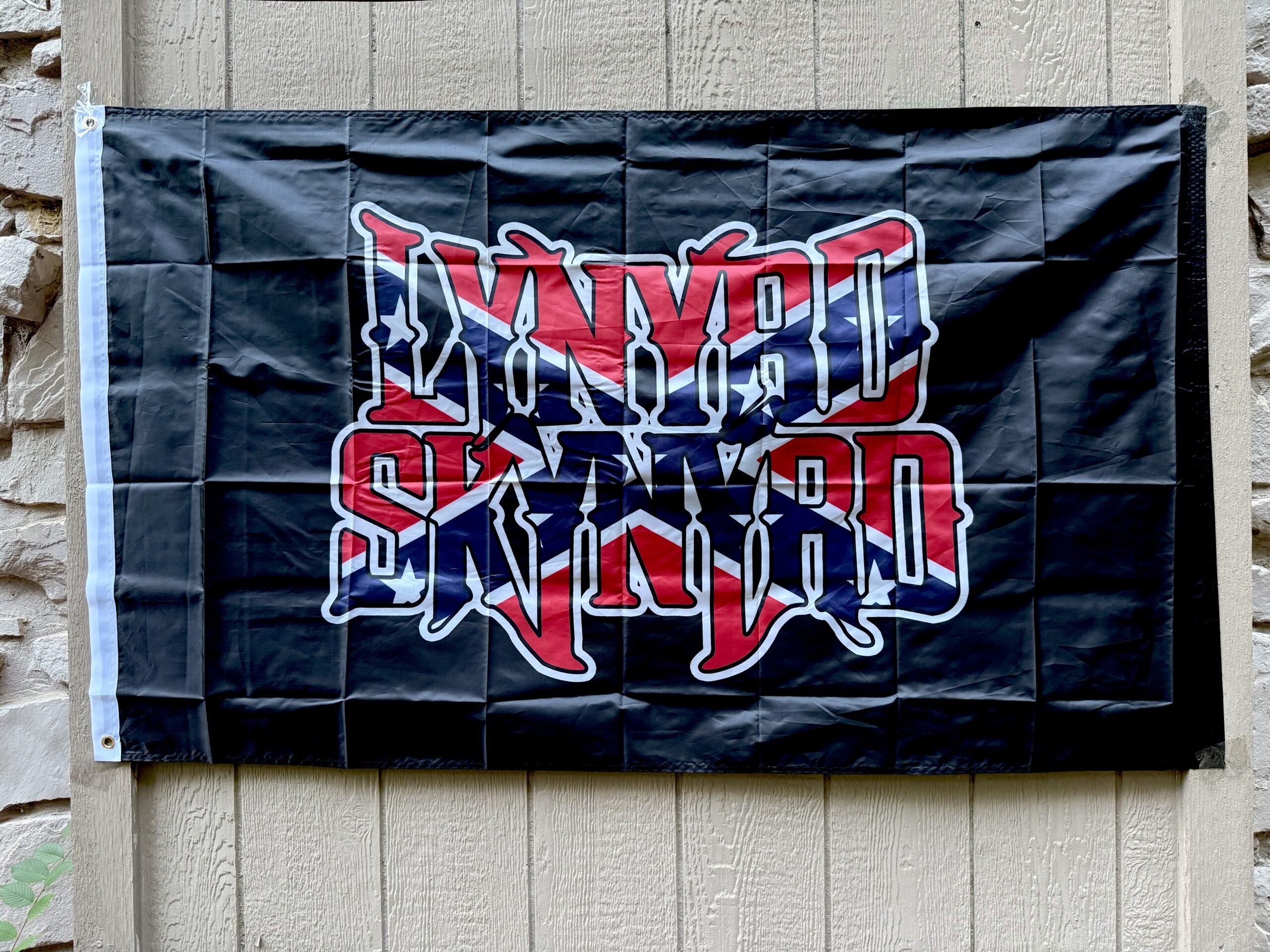 Lynyrd Skynyrd Confederate Flag with bold red, white, and blue logo on black background, displayed outdoors – Southern rock tribute banner.